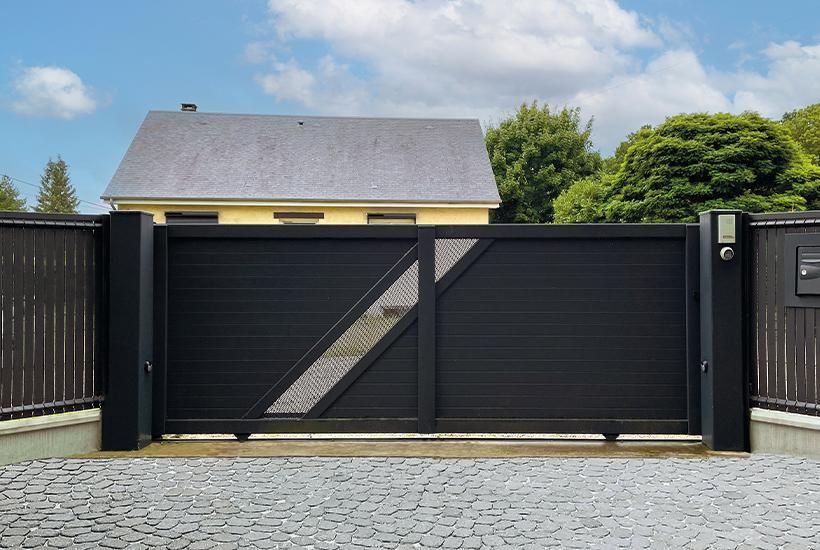 Portail coulissant aluminium noir fermé entre deux piliers, devant une allée pavée
