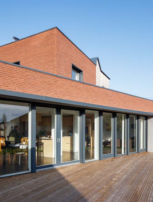 Maison en brique avec une série de baies coulissantes en bois sur la terrasse